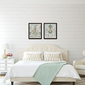 May include: A white upholstered bed with a light blue throw blanket and two framed prints of floral designs above the headboard. The bed is in a bedroom with white walls and a white wood floor. There is a white nightstand with a lamp and flowers on it to the left of the bed. A white armchair with a beige pillow is to the right of the bed.