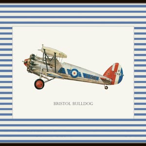 May include: Framed print of a vintage Bristol Bulldog biplane. The aircraft is painted in silver, white, red, and blue, with a roundel on the fuselage and tail. The print is set against a cream background, framed with a blue and white striped border.