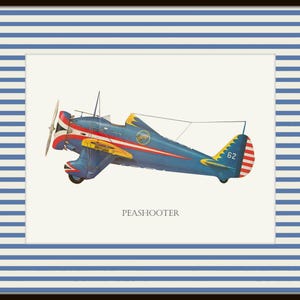 May include: A framed print featuring a vintage blue and red Peashooter airplane illustration. The plane has yellow accents and a propeller. The print is set against a white background and framed with a blue and white striped border.