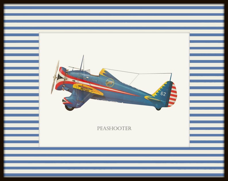 May include: A framed print featuring a vintage blue and red Peashooter airplane illustration. The plane has yellow accents and a propeller. The print is set against a white background and framed with a blue and white striped border.