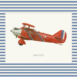 May include: A framed print of a vintage red biplane with blue and white accents. The biplane has a silver propeller and the word "BREGUET" is printed below the plane. The frame has a blue and white striped pattern.