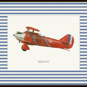 May include: A framed print featuring a vintage red biplane with blue and white accents. The biplane has a silver propeller and the word "BREGUET" is printed below the plane. The frame has a navy blue border with white and blue stripes.