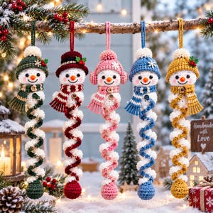 Op de afbeelding: Vijf gehaakte sneeuwpopornamenten hangend aan een tak. Elke sneeuwpop draagt een muts en sjaal in groen, donkerrood, roze, blauw of geel, met een lang, spiraalvormig wit en gekleurd lichaam dat eindigt in een bijpassende gehaakte bal.