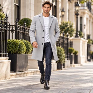 May include: A light gray overcoat with a notched lapel and three black buttons, worn over a plain white t-shirt and dark blue denim jeans. The ensemble is completed with black leather boots, creating a clean and structured appearance.