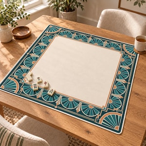 May include: A square mahjong mat with a cream-colored center and a decorative border featuring teal fan-shaped patterns and tan accents. Four small white mahjong tiles with red and green symbols are placed on the mat surface.