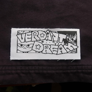 May include: A white patch with black line art of a cartoon character with the text "VERDANT DREAM" and a star.