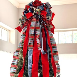 May include: A Christmas tree topper featuring a large bow with long cascading ribbons in red velvet, blue velvet, and a red, green, and blue plaid pattern. The topper includes red berries and a red flower. Text reads: FRONT VIEW 9 FOOT TREE.
