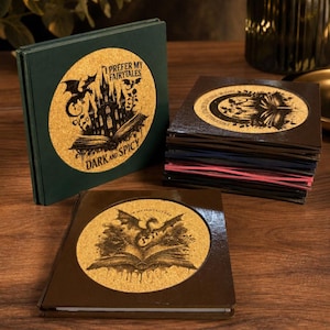 May include: A collection of square coasters with dark green, brown, and black frames. Each coaster features a circular cork inlay with black ink illustrations of dragons, castles, and open books. Text on the coasters reads I PREFER MY FAIRYTALES DARK AND SPICY and IN MY FANTASY ERA.