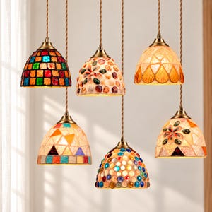 May include: A set of five hanging pendant lights with dome-shaped shades featuring various decorative designs including colorful mosaic tiles, embedded seashells, amber-toned glass patterns, and circular glass beads, all suspended by brown cords.