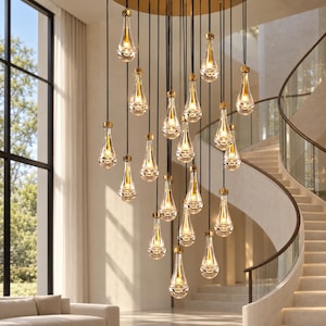 May include: A multi-light chandelier featuring numerous clear, teardrop-shaped glass pendants suspended at varying heights by thin black cords from a circular gold ceiling mount, each containing a small, warm-toned light source.