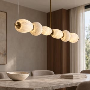 May include: A linear pendant light fixture featuring six illuminated, oval-shaped, textured white glass globes arranged horizontally along a central brass-toned metal rod, suspended from the ceiling by thin wires in a dining room setting.