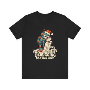 May include: A black t-shirt featuring a graphic of a blue robot wearing a red Santa hat, using a magnifying glass to inspect a long paper scroll with a small bug on it. Below the illustration, the text reads: DEBUGGING SANTA'S LIST.