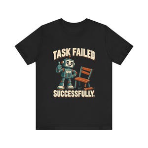 Peut inclure: Un t-shirt noir avec un motif représentant un robot bleu et gris faisant un pouce levé à côté d'une chaise en bois cassée. Le texte au-dessus du robot indique TASK FAILED et le texte en dessous indique SUCCESSFULLY dans une police claire.