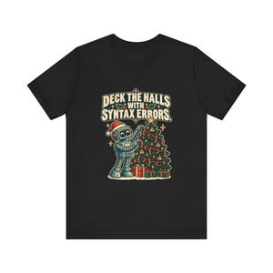 May include: A black t-shirt featuring a graphic of a grey robot wearing a red Santa hat, decorating a Christmas tree with red curly brackets and warning symbols. The text above reads DECK THE HALLS WITH SYNTAX ERRORS in a cream-coloured font.