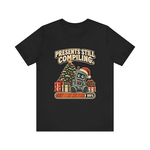 May include: A black t-shirt featuring a graphic of a robot wearing a Santa hat sitting in front of a Christmas tree and wrapped gifts. The text reads PRESENTS STILL COMPILING. Below the robot is a loading bar that is filled to 99 percent capacity.