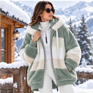 May include: A zip-up hooded jacket featuring a color-blocked pattern of sage green, cream, and beige in a plush, textured fleece material. The jacket includes a full-length front zipper, ribbed cuffs, and a drawstring hood, worn over a white turtleneck.