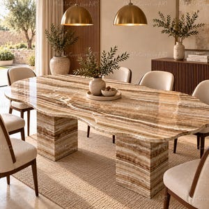 Puede incluir: Una mesa de comedor grande de forma ovalada hecha de piedra ónix pulida con bandas marrones y beige. La mesa presenta una superficie lisa de bordes orgánicos sostenida por dos pedestales rectangulares macizos del mismo material.