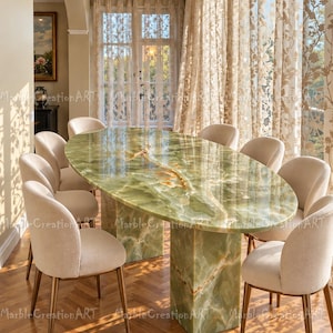 Peut inclure: Une table à manger ovale dotée d'un plateau en onyx vert poli avec des veines naturelles blanches et orange, reposant sur un pied central en onyx vert assorti, entourée de huit chaises rembourrées en tissu beige clair et pieds en métal.