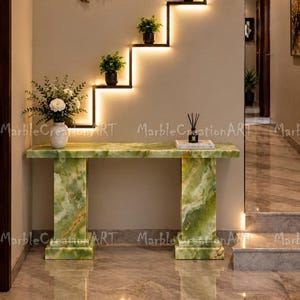 May include: A rectangular green onyx console table with two thick, matching stone legs. On the table sits a white vase with white flowers and a small black reed diffuser. Above the table is a stepped, wall-mounted shelf with integrated LED lighting.