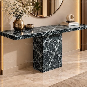 May include: A black marble console table with white veining features a rectangular top supported by a single central pedestal base. A gold vase with white flowers, a small bowl, and a stack of books with a sculpture sit on top.