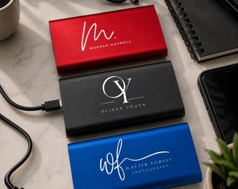 以下が含まれることがあります： 赤、黒、青の3つの長方形のモバイルバッテリー。それぞれに白いロゴと名前が印刷されています。赤いバッテリーにはM. Morgan Maxwell、黒いバッテリーにはOY Oliver Youth、青いバッテリーにはwf Walter Forest Photographyと記されています。