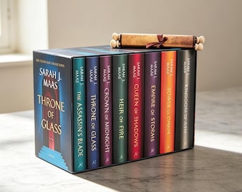 May include: A boxed set of eight hardcover books by Sarah J. Maas titled Throne of Glass, featuring colourful spines in teal, blue, purple, green, red, violet, orange, and black. A rolled parchment scroll tied with a brown ribbon rests on top.