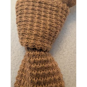May include: A solid brown necktie featuring a textured knit construction. The tie displays a consistent woven pattern throughout its length, showcasing a dense, uniform stitch design in a warm, earthy brown tone with a classic pointed end.