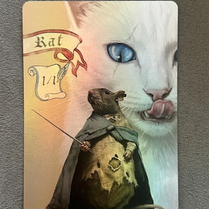 Op de afbeelding: Een rechthoekige ruilkaart met een bruine rat in een gehavende mantel die een dunne stok vasthoudt. Op de achtergrond is een grote witte kat met blauwe ogen zichtbaar. De tekst "Rat" staat op een banier en "1/1" op een perkamentrol.