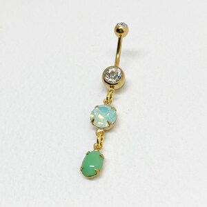 May include: Gold body jewelry with a chain and three crystals. The top crystal is clear, the middle crystal is light blue, and the bottom crystal is green.