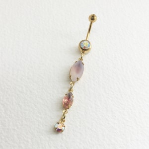 May include: Gold body jewelry with a pink, oval-shaped gemstone and smaller, iridescent gemstones.