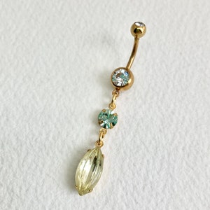 May include: Gold body jewelry with a clear gem at the top and a dangling chain with three green and clear gems.