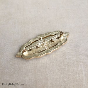 May include: Gold-toned metal brooch with an intricate, openwork design. The brooch has a pin and catch closure on the back.
