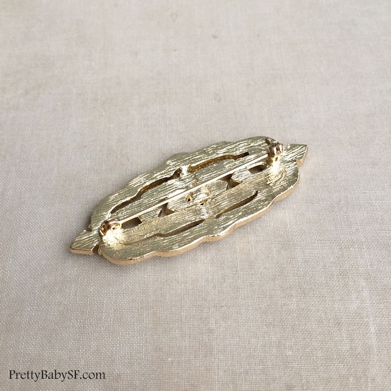 May include: Gold-toned metal brooch with an intricate, openwork design. The brooch has a pin and catch closure on the back.