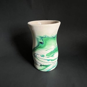 May include: A white ceramic vase with a green and blue marbled design. The vase has a wide mouth and a narrow base.
