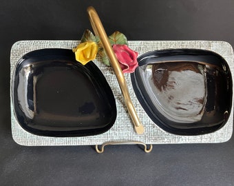 May include: A white ceramic serving tray with two black bowls and a gold handle. The tray has a textured surface and is decorated with three ceramic flowers: a yellow rose, a red rose, and a green leaf.
