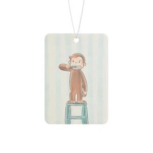 May include: A rectangular air freshener featuring a brown monkey standing on a light blue stool while brushing its teeth. The background consists of vertical light blue and white stripes. A thin white string is attached to the top for hanging.