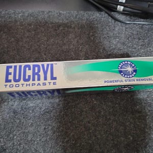 May include: A rectangular box of Eucryl toothpaste with a metallic silver finish. The front features the blue text EUCRYL TOOTHPASTE, a green graphic element, and a circular logo with the text FRESHMINT FLAVOUR and POWERFUL STAIN REMOVAL.