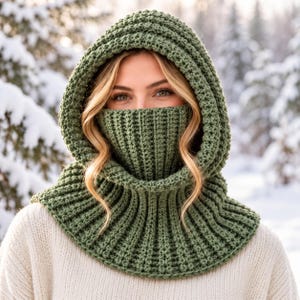 May include: A sage green crochet balaclava featuring a ribbed texture and an integrated hood. The head covering extends to cover the nose and mouth, with a wide, flared ribbed collar that rests over the shoulders and chest area.