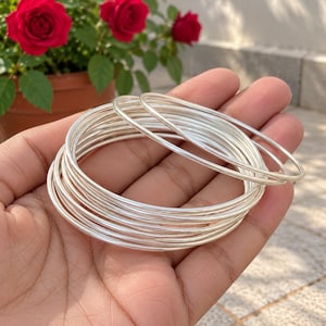 Peut inclure: Un empilement de plusieurs bracelets joncs fins et polis de couleur argentée avec une surface lisse et arrondie. Les bracelets sont de forme circulaire et présentent une finition métallique réfléchissante, créant un aspect superposé.