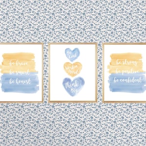 May include: Three watercolor prints with inspirational messages. The first print has a blue and yellow watercolor background with the text "be brave, be smart, be honest". The second print has three watercolor hearts with the text "Be Kind, Work Hard, Think Big". The third print has a blue and yellow watercolor background with the text "be strong, be positive, be confident".
