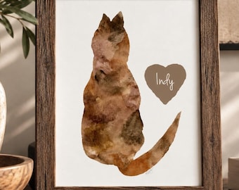 May include: A rectangular wooden frame containing a white print of a cat silhouette rendered in brown and tan watercolor textures. To the right of the cat is a brown heart shape with the name Indy written in white script lettering.