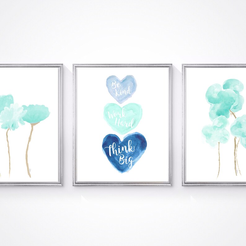 May include: Three watercolor prints in silver frames. The left print features two light blue flowers with gold stems. The center print features three watercolor hearts in shades of blue with the text "Be Kind, Work Hard, Think Big". The right print features three light blue watercolor clouds with gold stems.