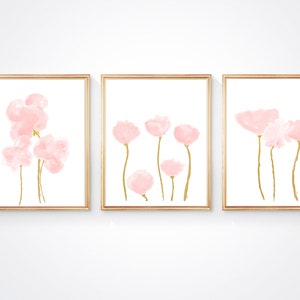 Pu&ograve; includere: Tre stampe incorniciate con fiori rosa in stile acquerello e steli dorati su sfondo bianco.