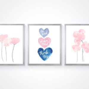 May include: Three framed watercolor prints with a white background. The center print features three watercolor hearts in shades of blue and pink with the text "Be Kind", "Work Hard", and "Think Big". The prints on either side feature a single watercolor flower in shades of pink.