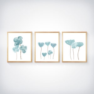 Pu&ograve; includere: Set di tre stampe ad acquerello incorniciate con fiori blu astratti. Le stampe sono in semplici cornici dorate e hanno uno sfondo bianco.
