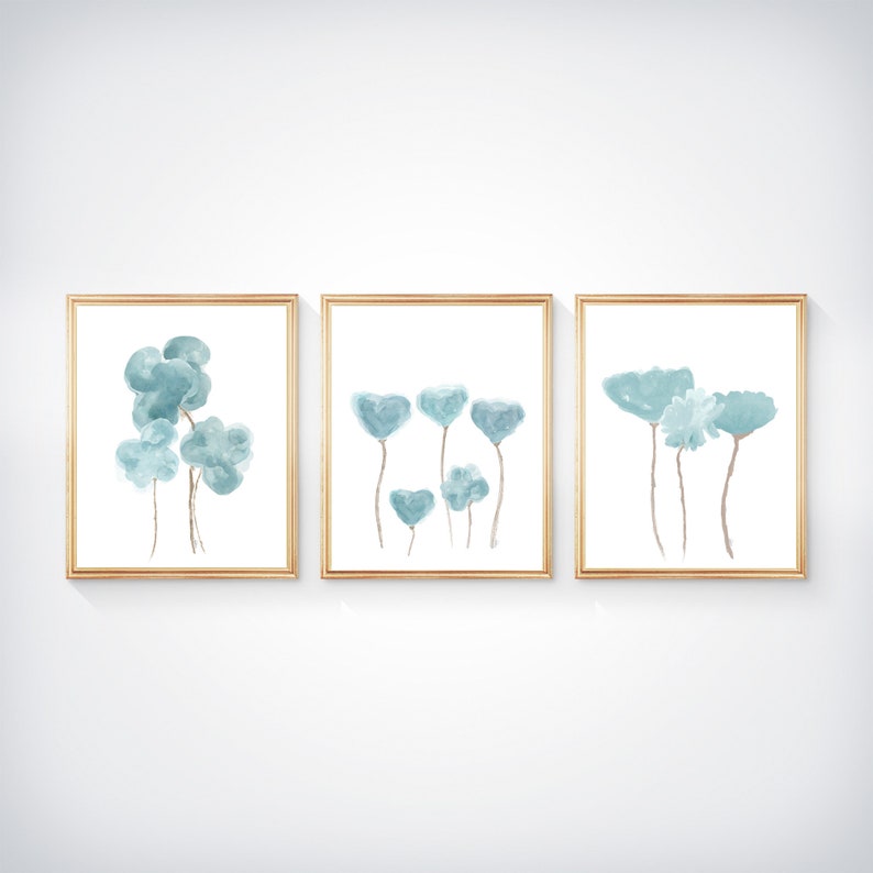 Pu&ograve; includere: Set di tre stampe ad acquerello incorniciate con fiori blu astratti. Le stampe sono in semplici cornici dorate e hanno uno sfondo bianco.