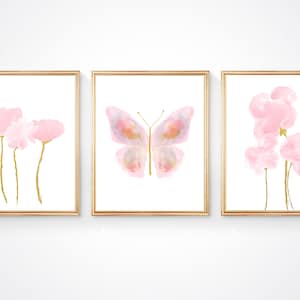 May include: Set of three watercolor prints featuring pink flowers and a butterfly with gold accents. The prints are framed in gold.