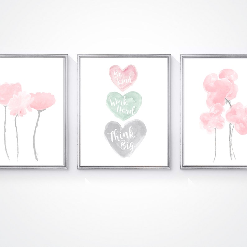 May include: Three watercolor prints in silver frames. The center print features three watercolor hearts with the words "Be Kind", "Work Hard", and "Think Big". The prints on either side feature pink watercolor flowers.
