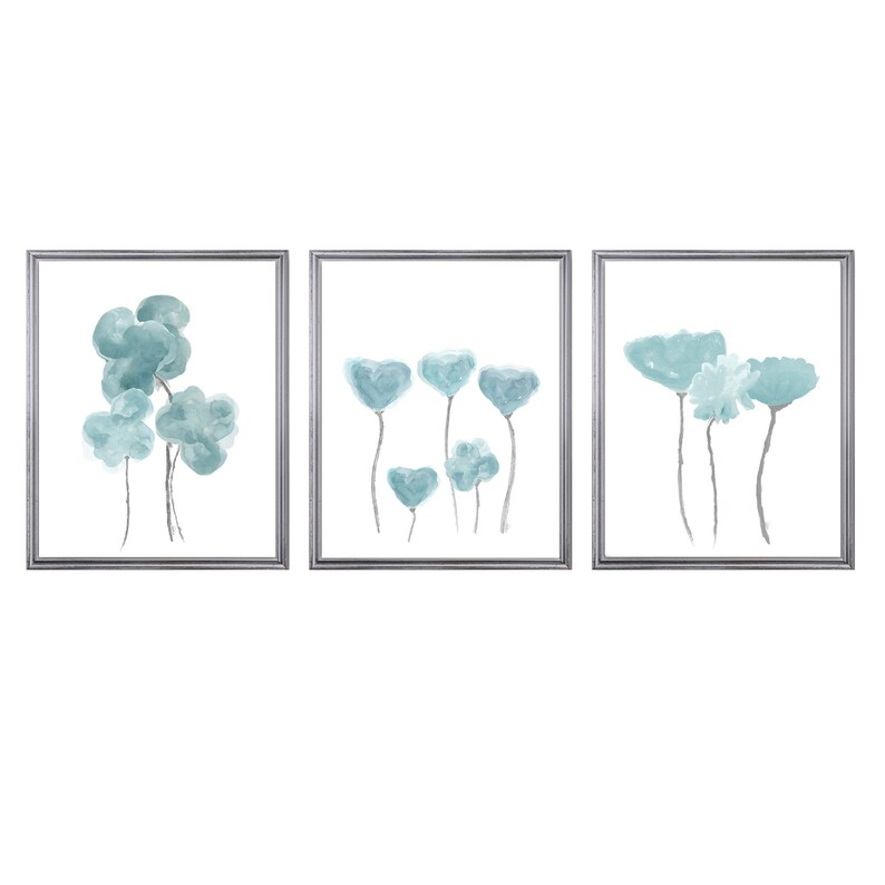 Pu&ograve; includere: Set di tre stampe ad acquerello incorniciate con fiori blu astratti. Le stampe sono in cornici argentate e hanno uno sfondo bianco.