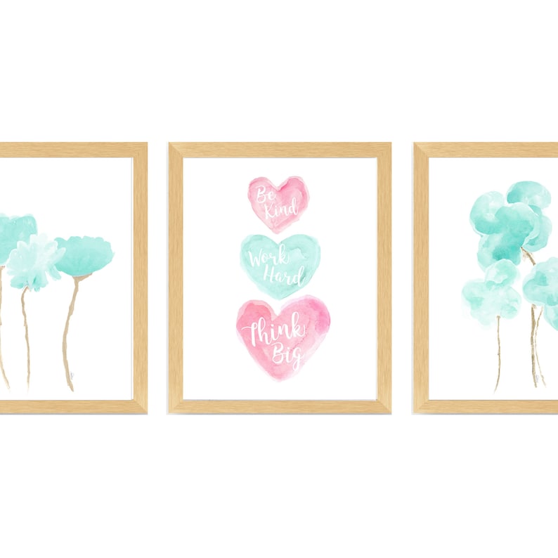 May include: Set of three framed watercolor prints with a light blue and pink color scheme. The first print features a cluster of light blue watercolor flowers. The second print features three stacked watercolor hearts with the words "Be Kind", "Work Hard", and "Think Big" written in white. The third print features a cluster of light blue watercolor clouds.